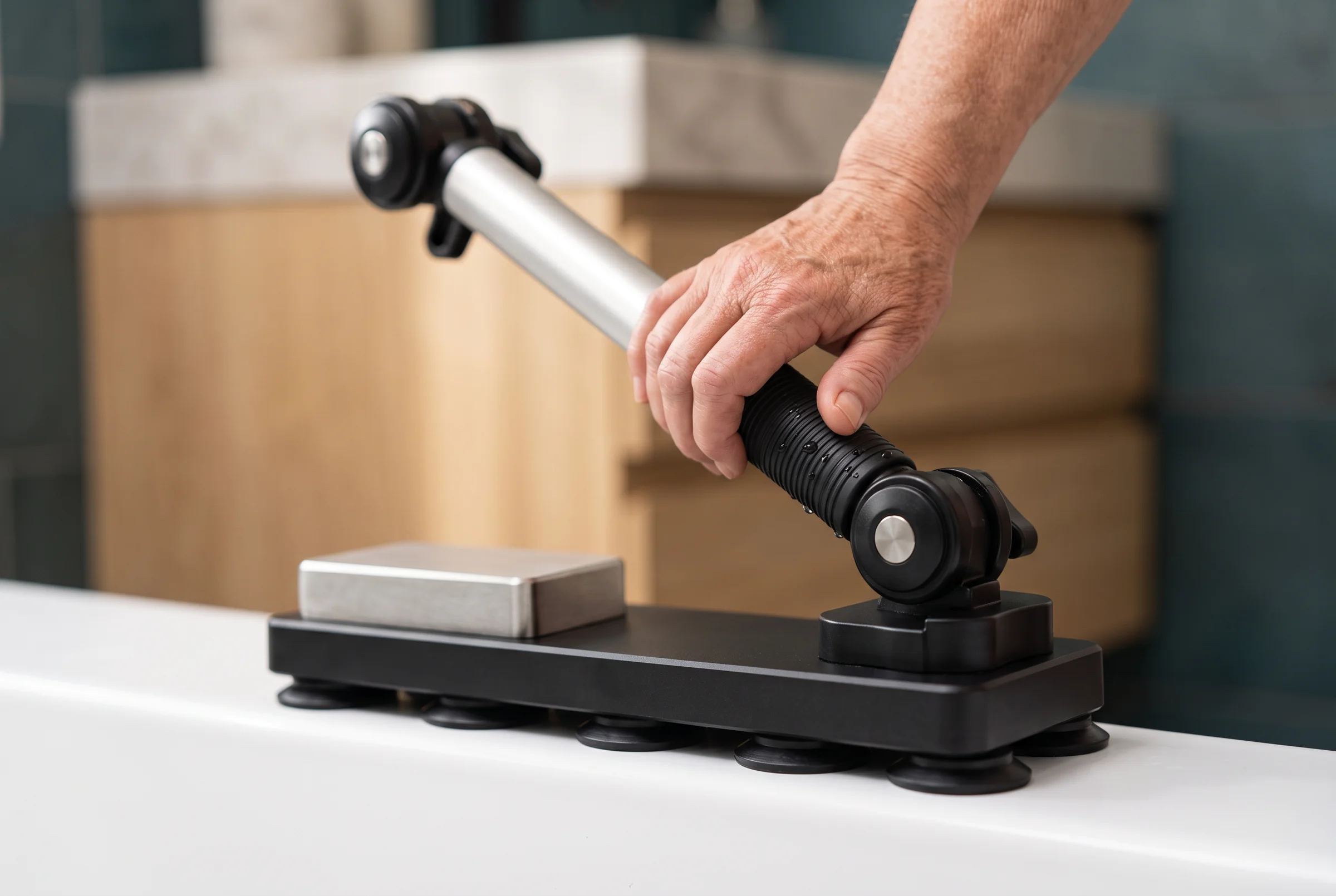 An older adult's hand resting on the bath support's ribbed grip.